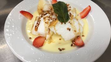 A white plate with a dessert consisting of white cake, strawberries, and a yellow sauce.