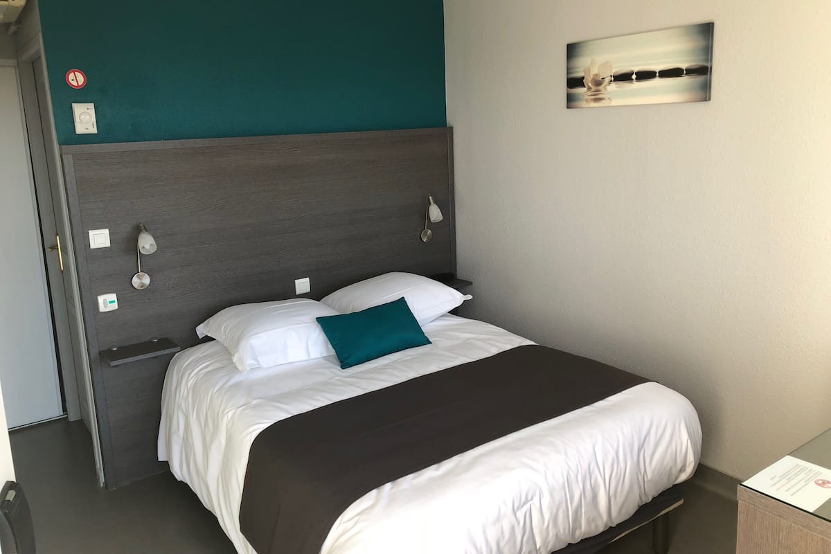 Una habitación de hotel con una cama, un pared decorada en color aguamarina, un cuadro y una mesita de noche.