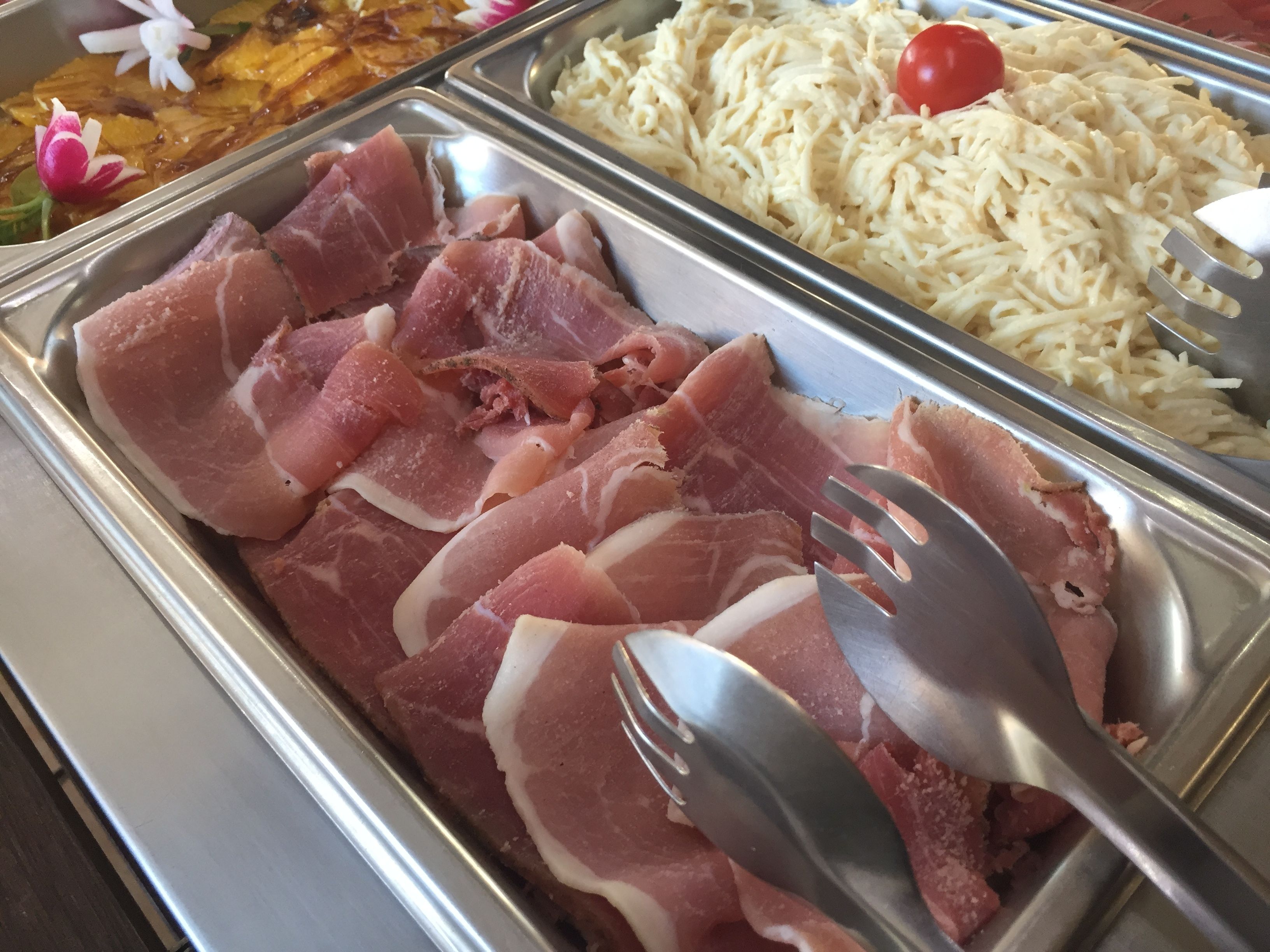 Un bufé con jamón en rodajas, queso rallado y tomate cherry.