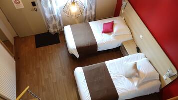 Ein Zimmer mit zwei Betten, Holzboden, roter Wand und einer Pendelleuchte.