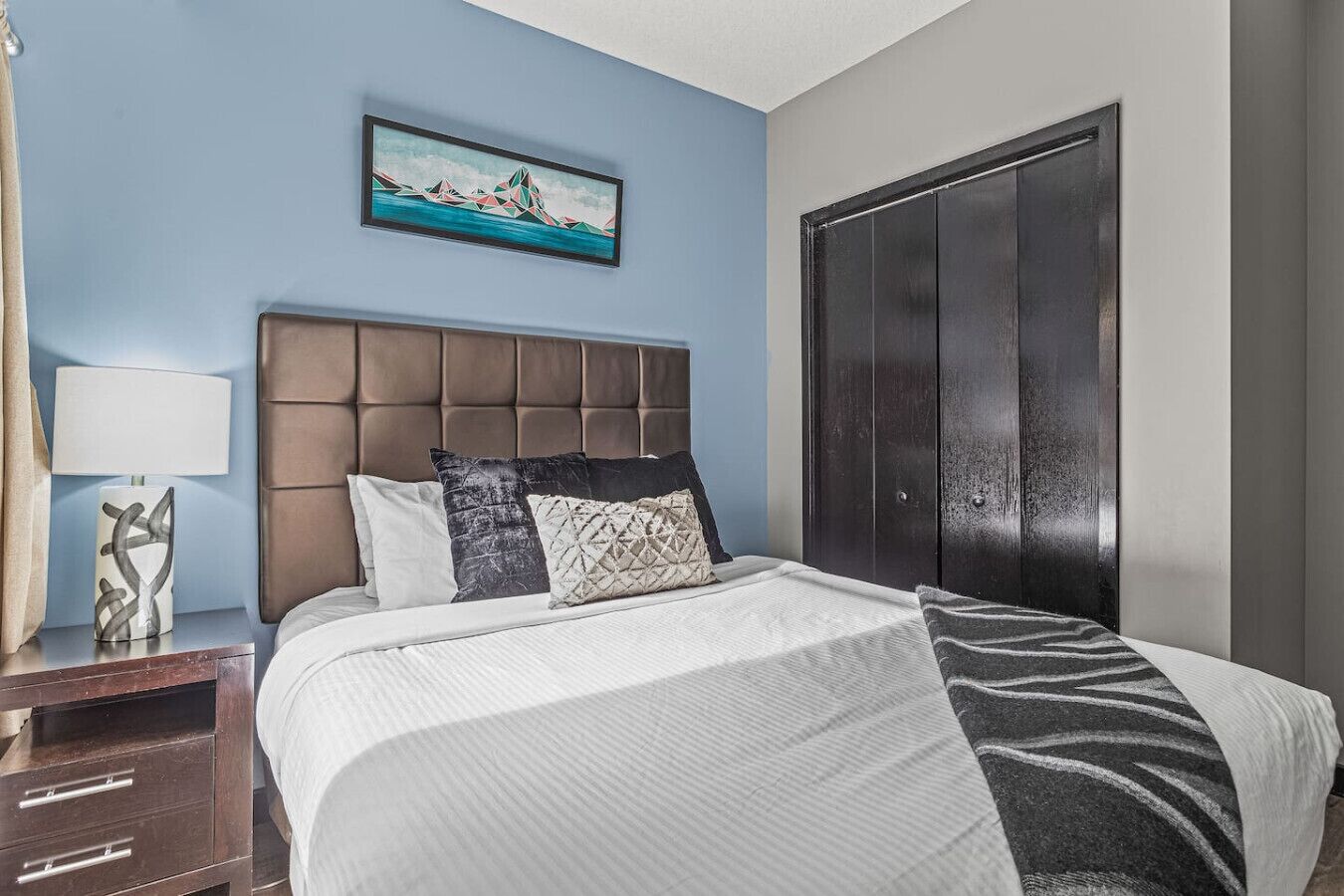 Une chambre d’hôtel avec un grand lit, une table de chevet avec une lampe, un tableau au mur et une armoire.