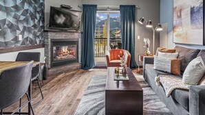 A modern living room with a fireplace, a dining area, and a sofa. - Experience Cozy Rockies Escape w/ Pool & Hot tub (Canmore)