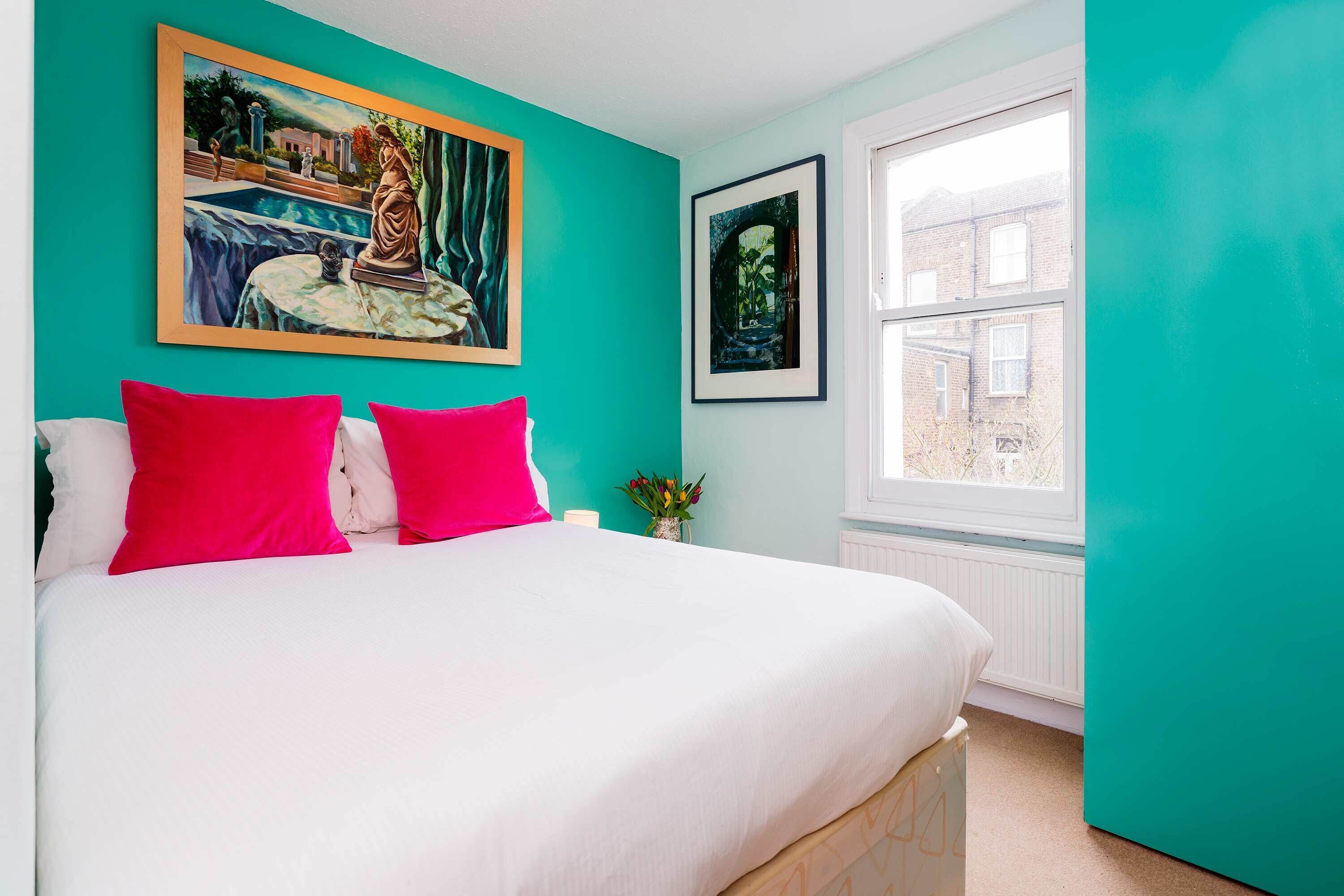 A bedroom with a bed, teal walls, a window, and two framed pictures.