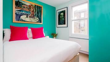 A bedroom with a bed, teal walls, a window, and two framed pictures.