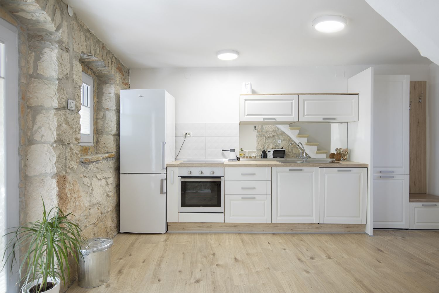 A modern kitchen with white cabinets, a built-in oven, and a stone wall.