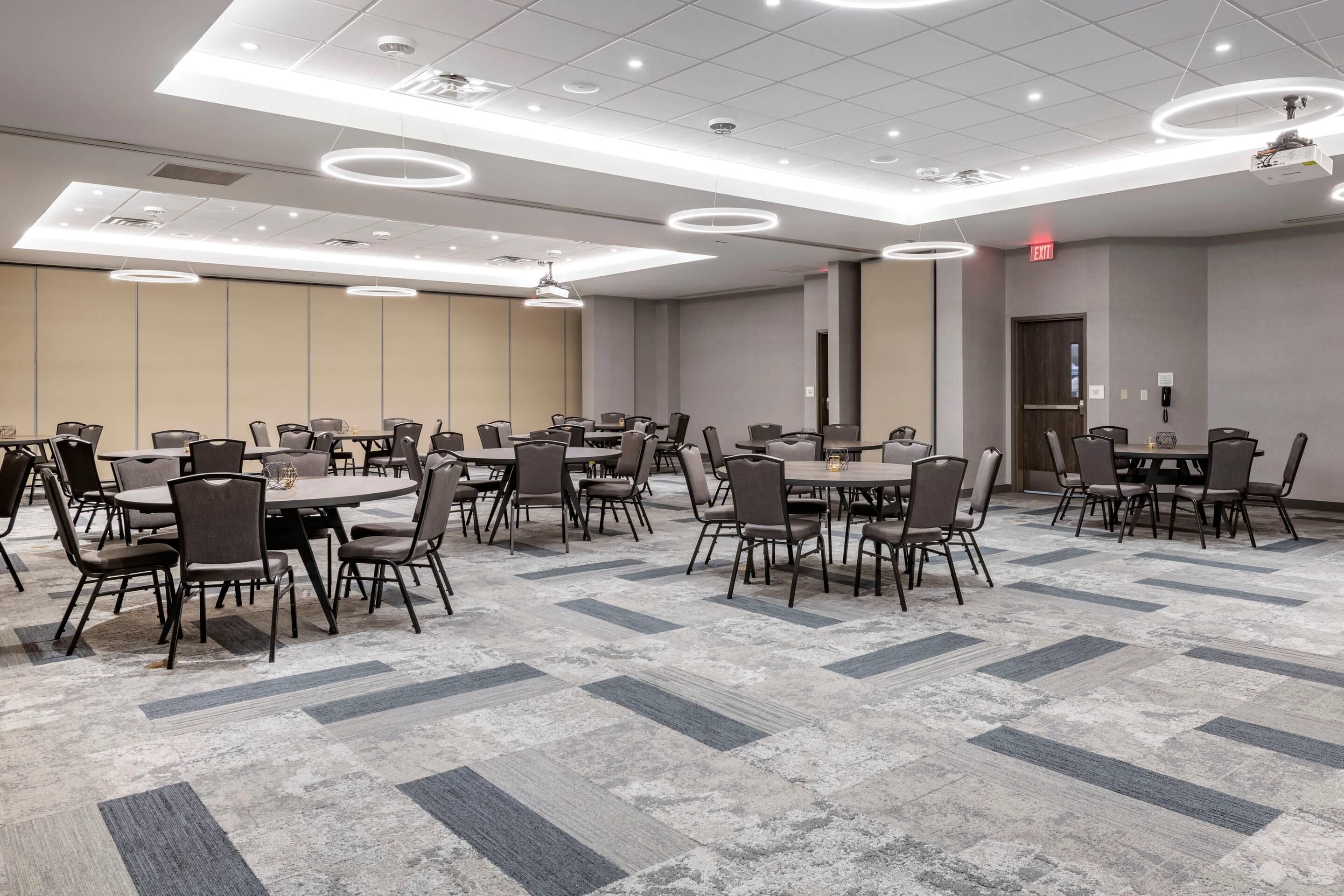 A conference room with multiple tables and chairs, ceiling lights, and a patterned carpet.