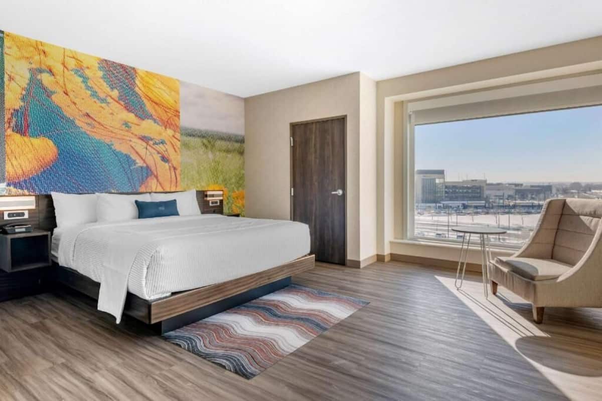 A modern hotel room with a large bed, a view of the city, and a large window.