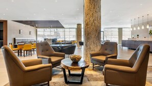 Un espacio lounge moderno con sillones de cuero, una mesa de centro redonda y un grueso pilar de madera.