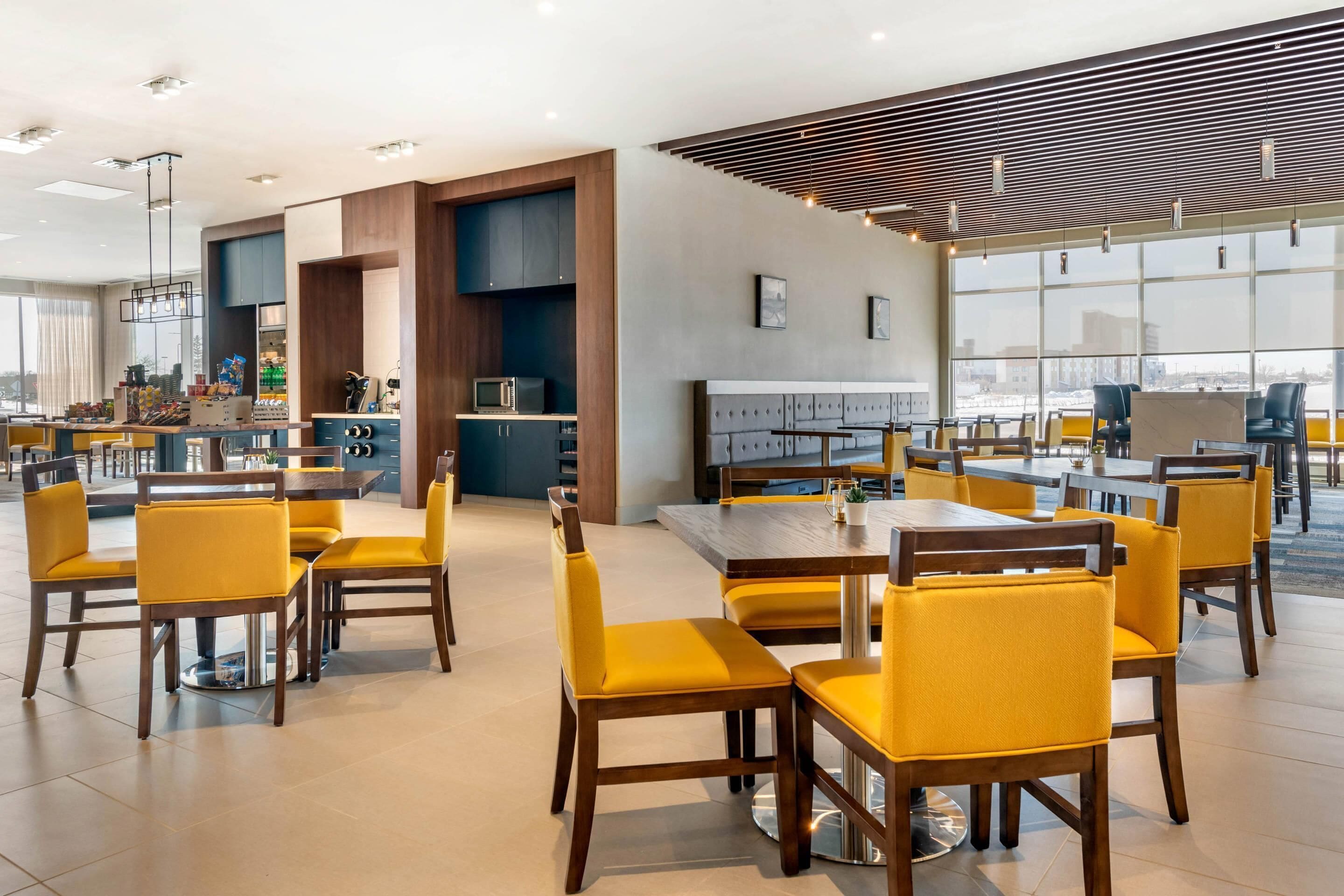 A modern dining area with yellow chairs, a central table, and a kitchen in the background.