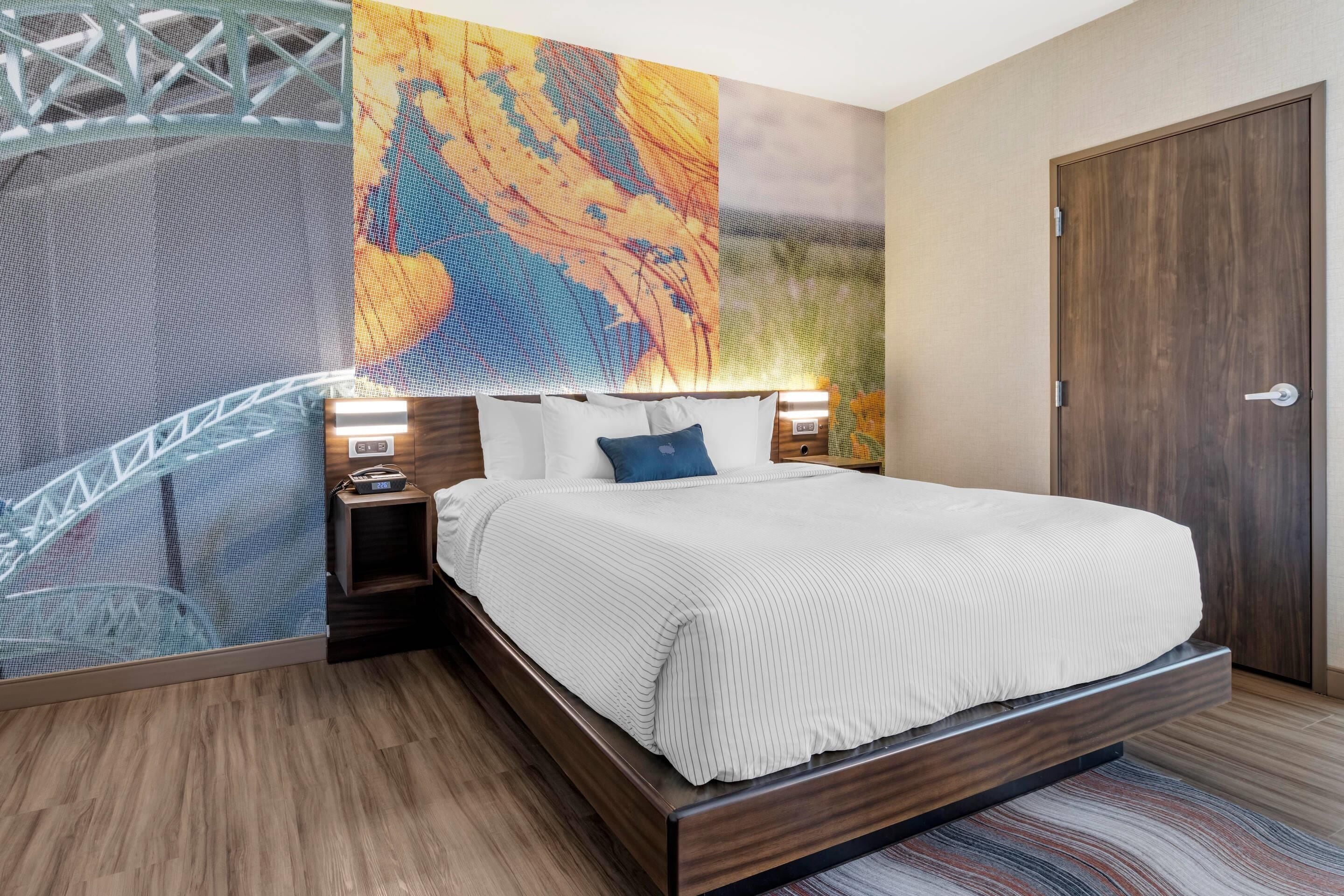 A bedroom with a bed, nightstands, a wooden door, and a wall with a large abstract painting.