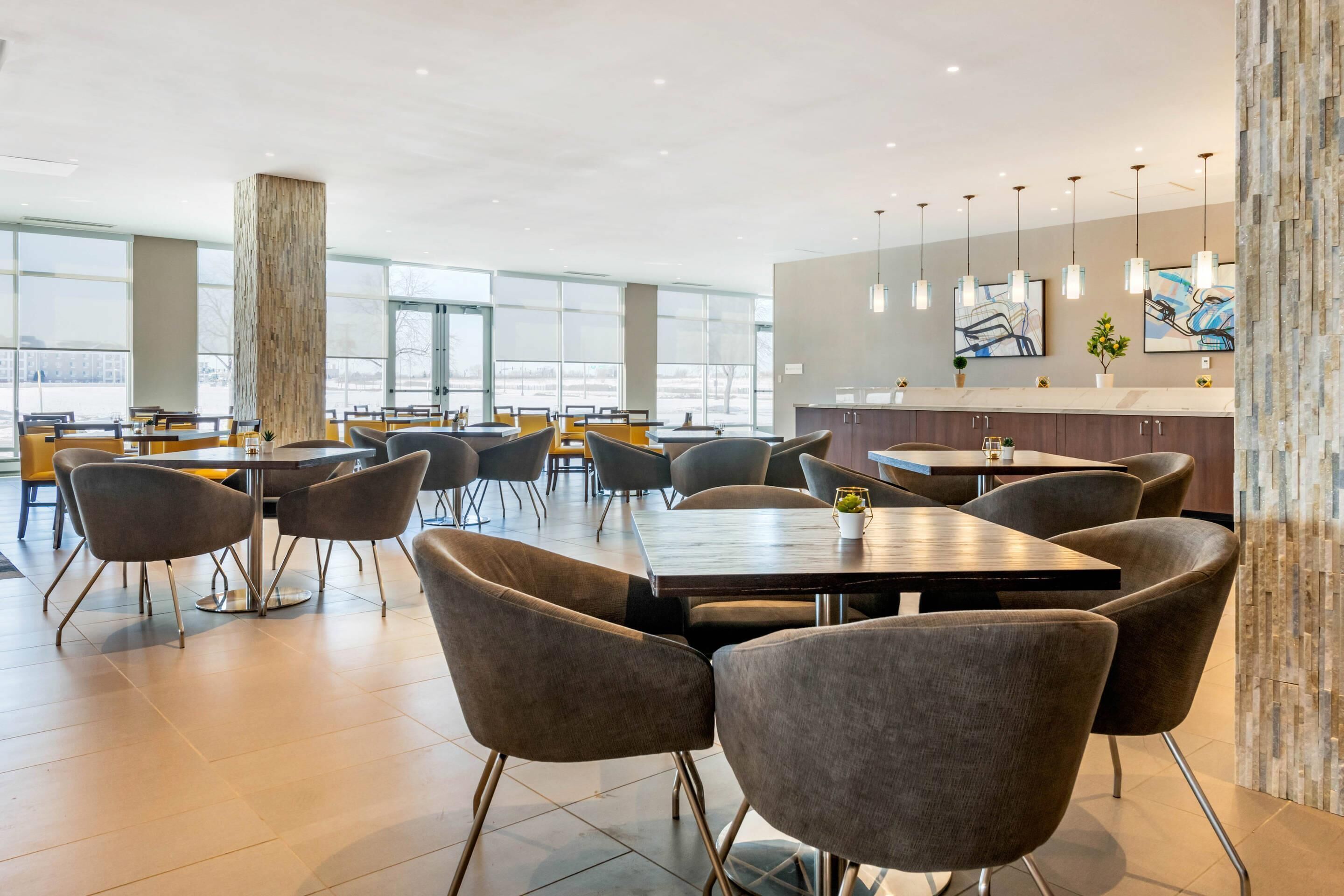 Un espace repas moderne avec des tables et des chaises, un comptoir de cuisine et de grandes fenêtres.
