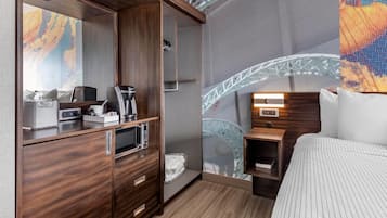 A hotel room with a wooden wardrobe, a bed with striped bedding, a small bedside table, a built-in microwave, and a large window with a view of a bridge.