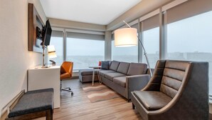 Una habitación de hotel moderna con sofá, sillón, escritorio y grandes ventanales con vistas a la ciudad.