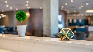 Una zona de recepción con mostrador de mármol, una planta en maceta y un moderno jarrón geométrico decorativo.