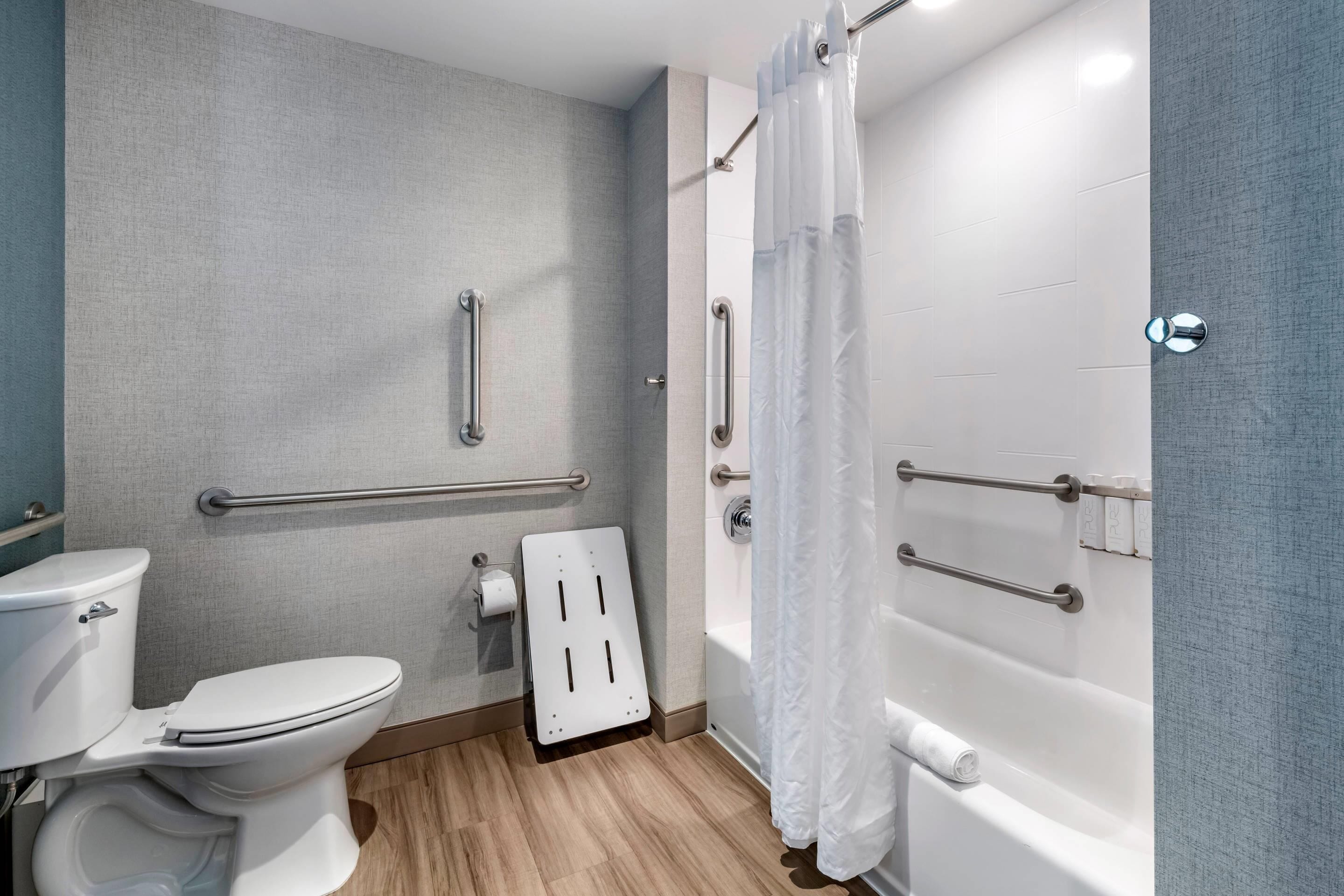 A bathroom with a toilet, a shower with a curtain, and handrails.