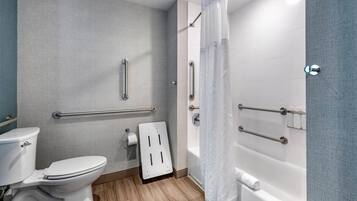 A bathroom with a toilet, a shower with a curtain, and handrails.