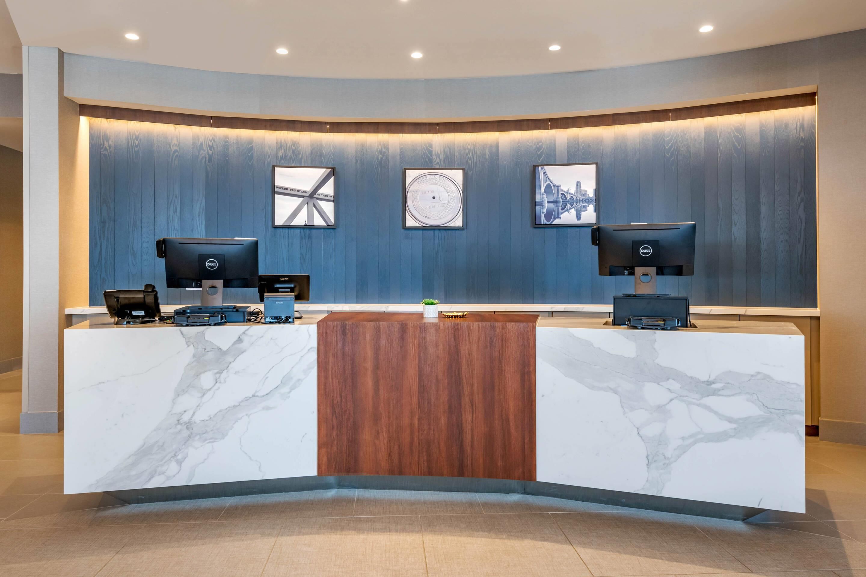 A reception desk with two monitors, a wooden panel, and three framed pictures on the wall.