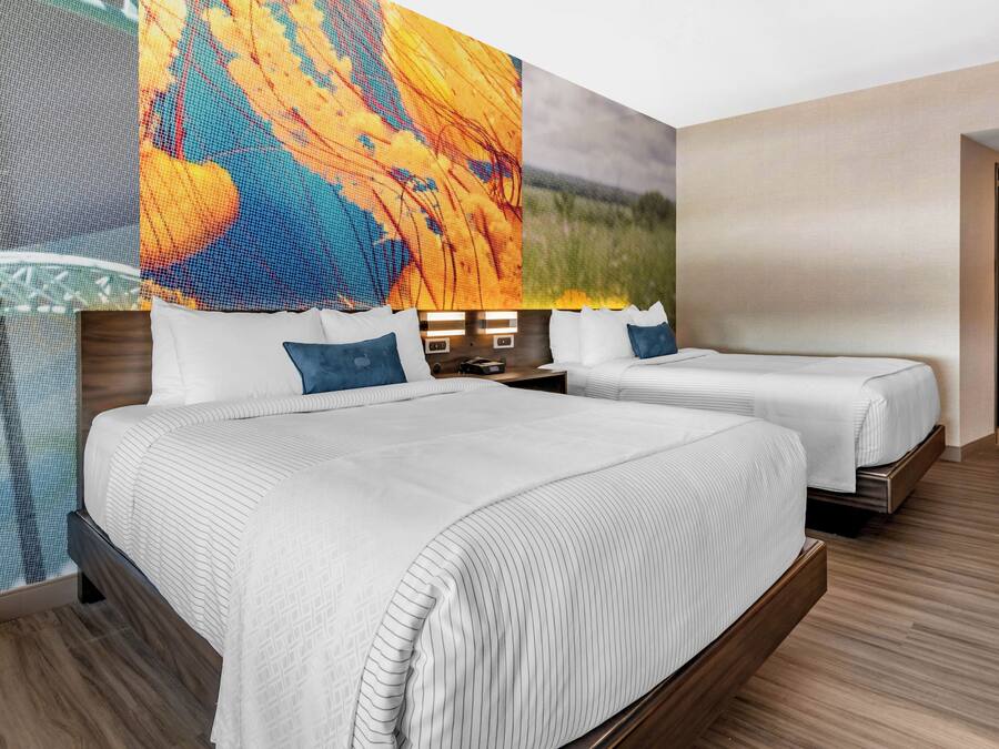 A hotel room with two beds, a large wall mural, and a wooden floor.