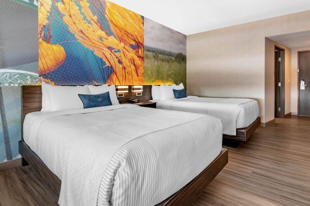 A hotel room with two beds, a large wall mural, and a wooden floor.