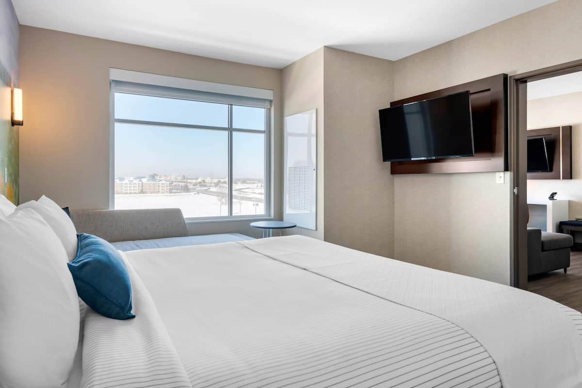 A hotel room with a large bed, a TV mounted on the wall, a window with a city view, and a small table.