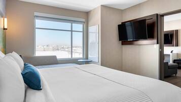 A hotel room with a large bed, a TV mounted on the wall, a window with a city view, and a small table.