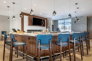 A modern kitchen with a central island, bar stools, pendant lighting, and a large window.
