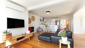 A modern living room with a flat-screen TV, wooden flooring, a leather sofa, and a small table with a plant. - Eight on Church Waiheke Accommodation (Waiheke Island)
