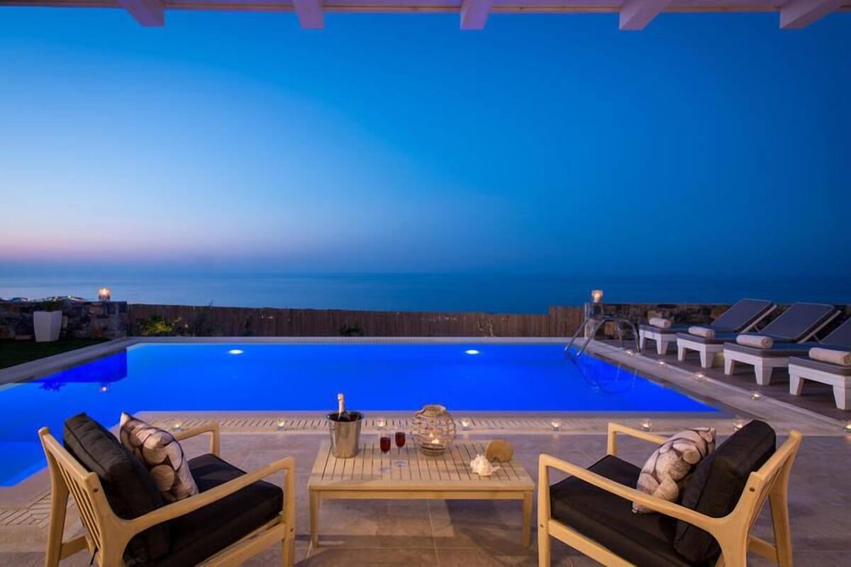 Ein Poolbereich mit Liegestühlen, einem Tisch mit Getränken und Blick auf den Ozean im Abendrot.