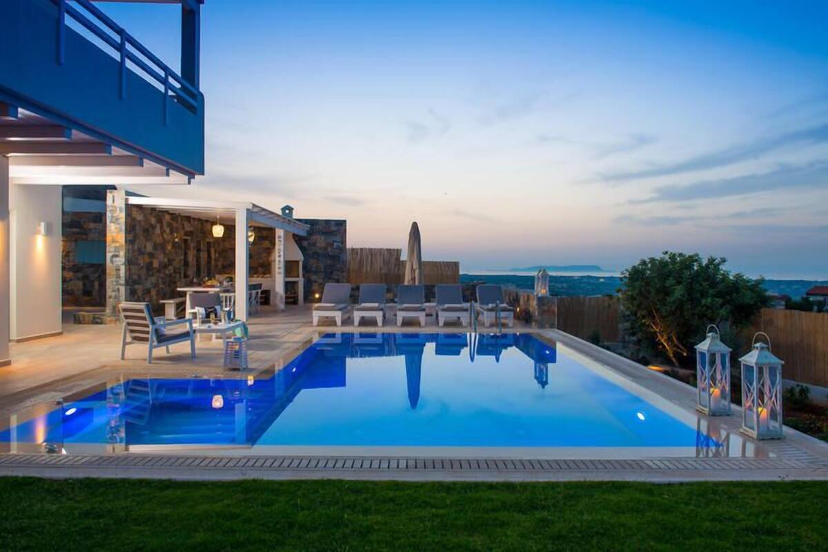 Ein moderner Poolbereich im Freien mit freiem Blick auf den Ozean, einer Steinmauer und einer Holzterrasse mit Liegestühlen.