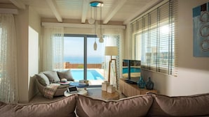 A living room with a sofa, a coffee table, a TV, and a pool view. - Villas Crete (Hersonissos)