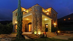 A stone house with a balcony, a staircase leading to the entrance, and a well-lit front porch. - Villas Crete (Hersonissos)