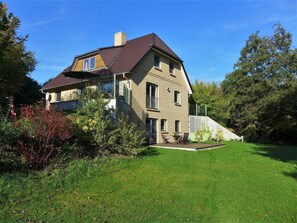 Une maison à deux étages, dotée d’un toit en pente, d’un balcon à l’étage supérieur et d’une pelouse bien entretenue.