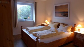 Un letto di legno con due cuscini e una coperta, una finestra con tende, un comodino con una lampada e un quadro appeso al muro.