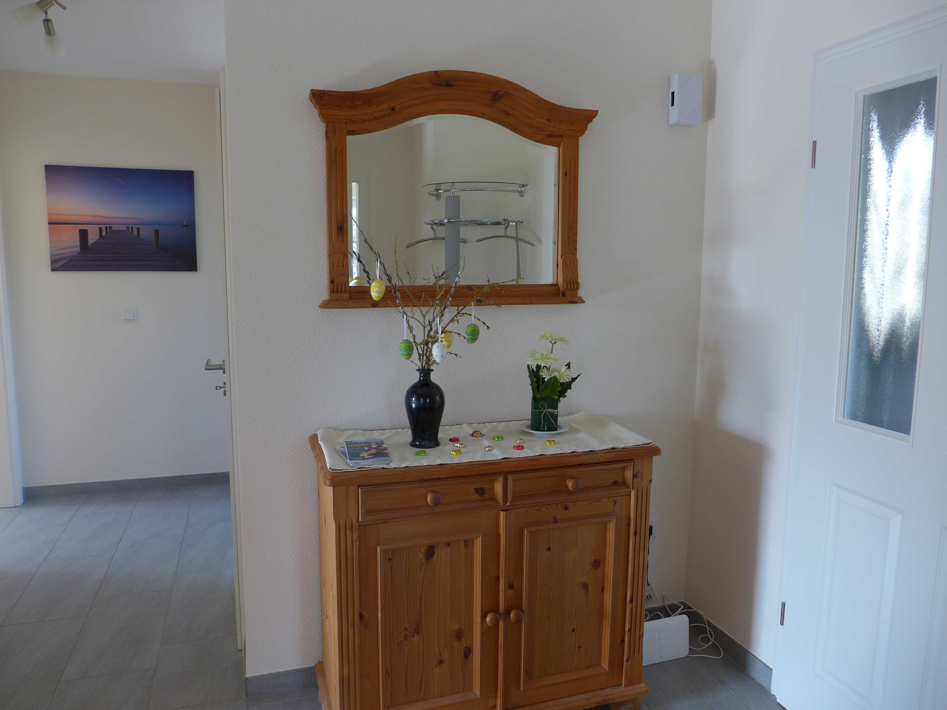Un mueble de madera con un espejo encima, un florero con flores y un cuadro en la pared.