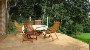 Une terrasse en bois avec une table et des chaises, entourée d’une clôture verte et d’arbres.
