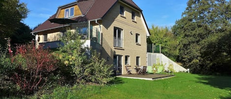 A two-story house with a sloped roof, a balcony on the upper floor, and a well-maintained lawn.
