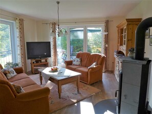 A living room with a TV, sofa, armchair, and a fireplace. - Apartments Schleibach - Apartments Hartmann (Rabenkirchen-Faulück)