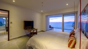 Quarto com cama grande, televisão, escrivaninha e varanda vista para o mar.