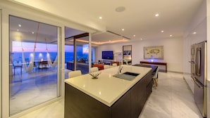 Uma cozinha moderna com uma ilha grande, uma área de refeições com vista e um espaço de estar com televisão e obras de arte.