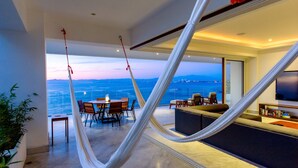 Uma sala de estar moderna com uma grande janela com vista para um corpo de água, uma rede, uma área de jantar e uma área de estar com televisão.