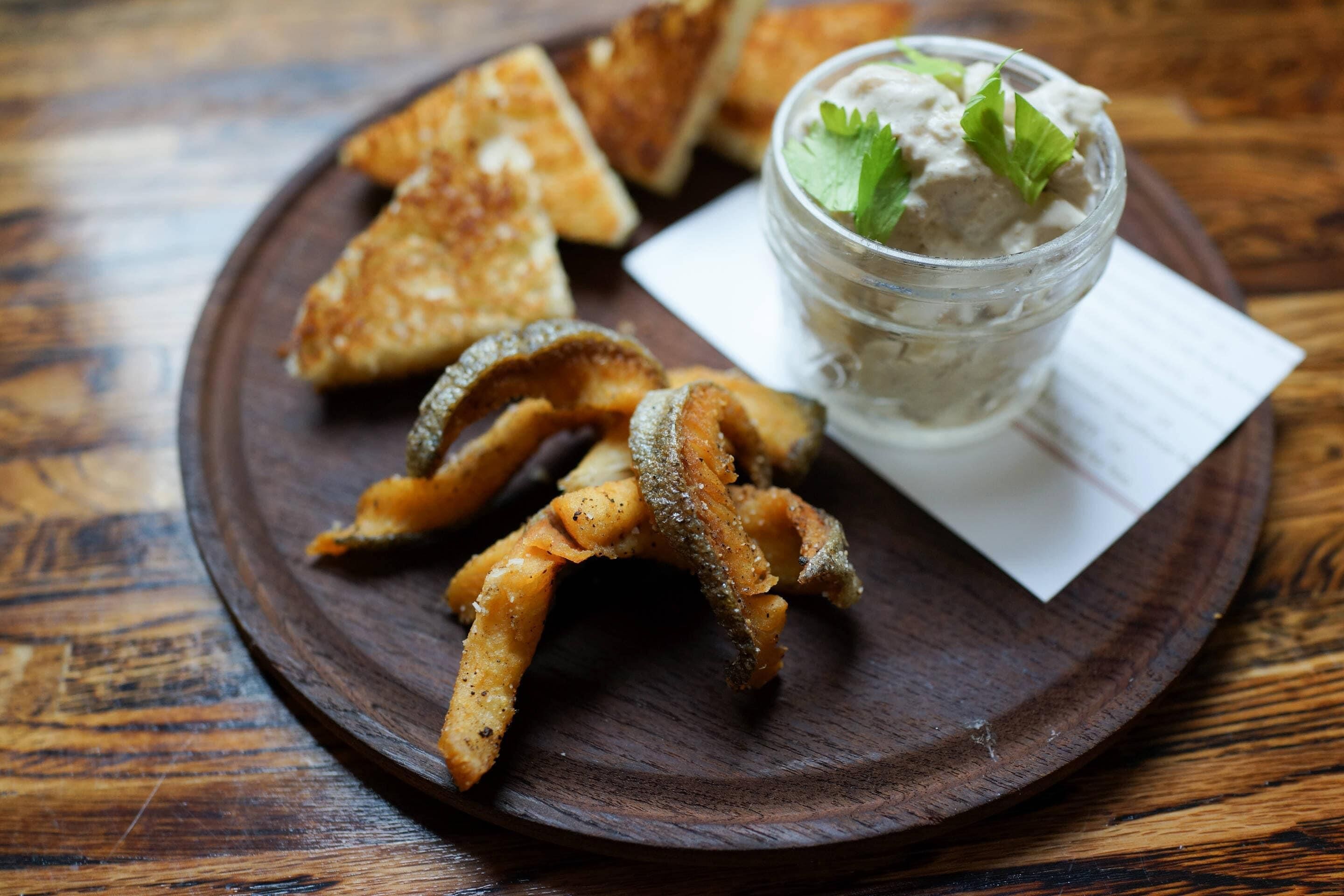 A wooden plate with fried items and a small jar of dip.