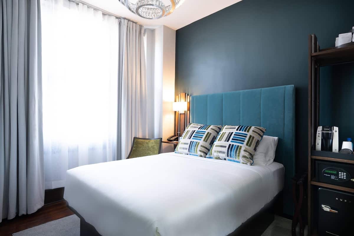 A hotel room with a large bed, a nightstand, a lamp, and a minibar.