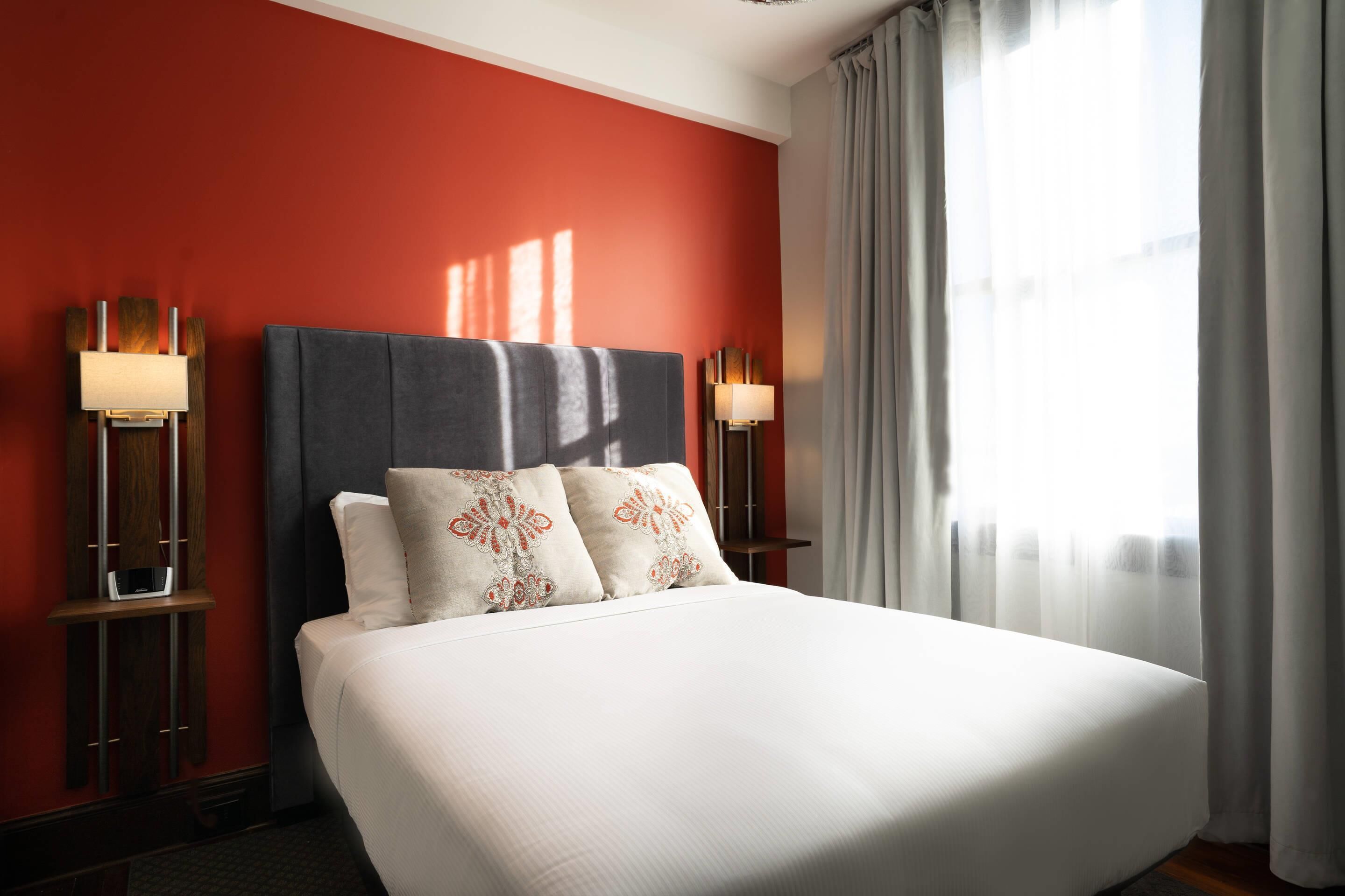 Una habitación de hotel con una cama grande, dos lámparas de noche y un ventanal con cortinas.