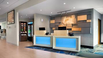 A hotel reception area with a modern design, including a digital display, a refrigerator stocked with beverages, and a clock on the wall.