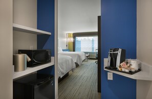 Quarto de hotel com cama, micro-ondas, máquina de café e um pequeno armário com artigos de higiene pessoal.