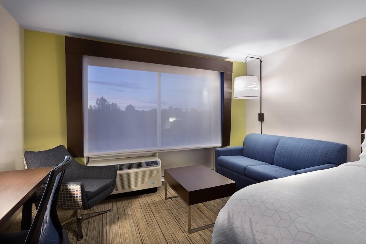 A hotel room with a large window, a sofa, a bed, a desk, and a chair.