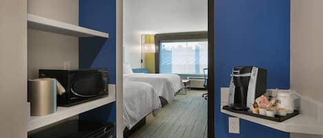 Habitación de hotel con cama, microondas, cafetera y un pequeño estante con artículos de aseo.