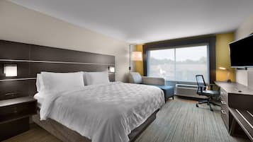 A modern hotel room with a large bed, a desk with a chair, a TV, and a window with a view.