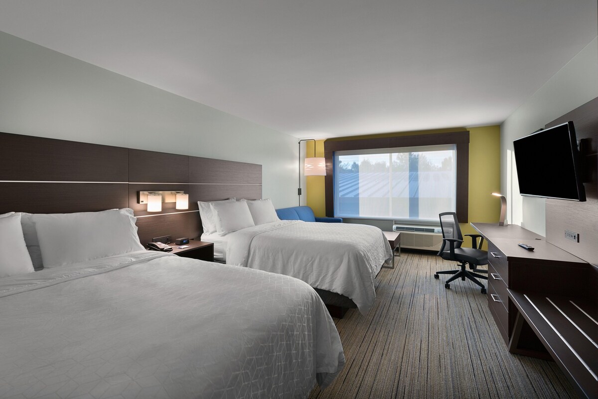 A hotel room with two beds, a desk, a chair, a TV, and a window with a view.