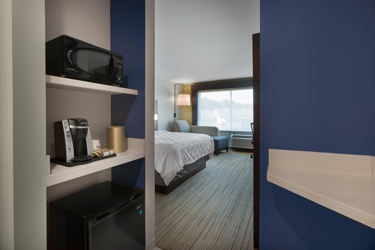 A hotel room with a bed, a microwave, a coffee maker, and a desk lamp.